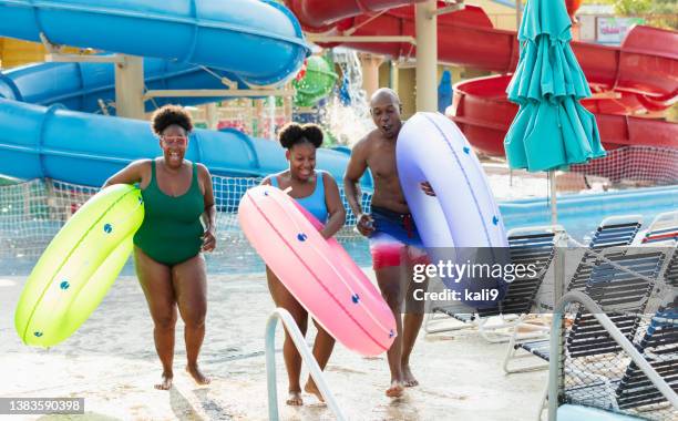 family at waterpark carry inflatable rings to lazy river - lazy river stock pictures, royalty-free photos & images