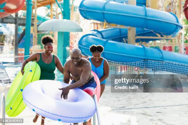 family at waterpark carry inflatable rings to lazy river - water slide stock pictures, royalty-free photos & images