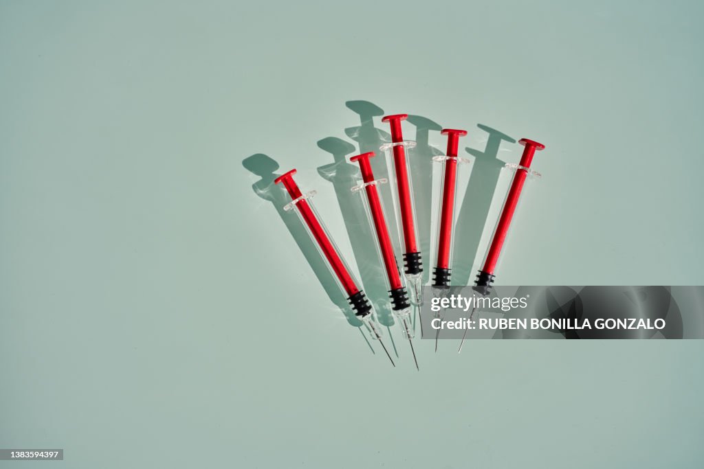 Medical empty red syringes with shadows organized in a pattern on blue background. Healthcare and medical concept.