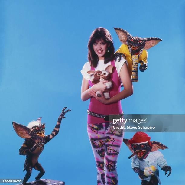 Portrait of American actress Phoebe Cates as she poses with several creatures, gremlins and mogwai , from the film 'Gremlins' , as she poses in front...