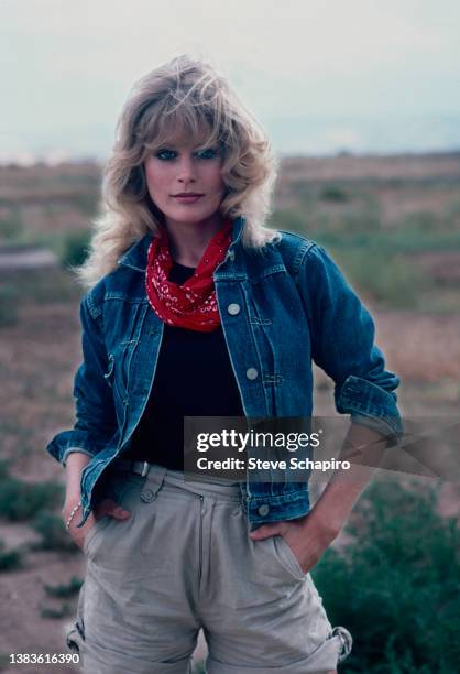 Portrait of American actress and singer Beverly D'Angelo wearing a blue denim jacket over a black top and a red neck scarf, her hands in the pockets...