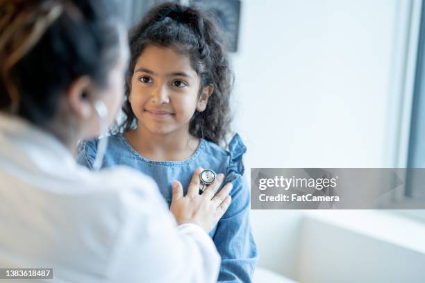 doctor listening to a young girls heart - huisarts stockfoto's en -beelden