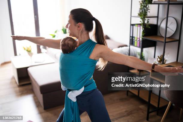 madre sosteniendo al bebé en cabestrillo y haciendo ejercicio en casa. - portabebés fotografías e imágenes de stock