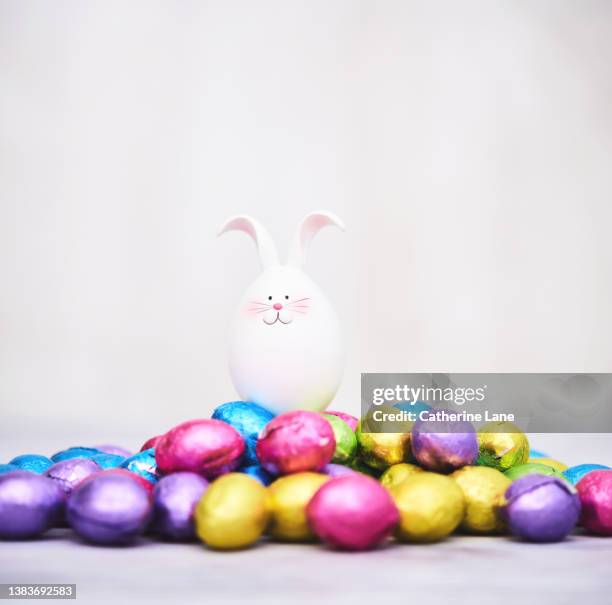 cute easter bunny sitting in a pile of foil covered chocolate eggs - chocolate bunny stock-fotos und bilder