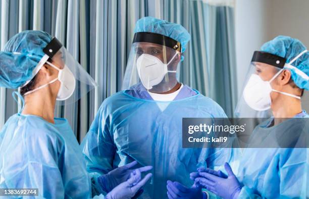 three healthcare workers wearing ppe, conversing - operating gown stock pictures, royalty-free photos & images