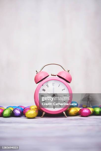 easter time. pink alarm clock with foil covered easter eggs. - spring forward fotografías e imágenes de stock