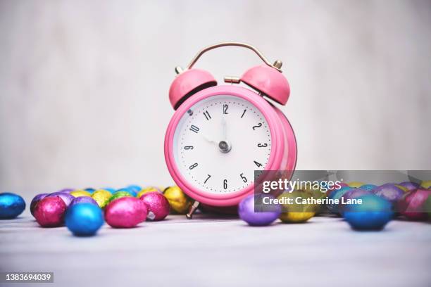 easter time. pink alarm clock with foil covered easter eggs. - spring forward stock pictures, royalty-free photos & images