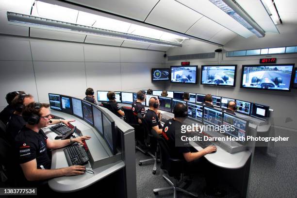 McLaren Formula One racing team engineers and analysts sitting in the Mission Control room as television screens show live television pictures –...
