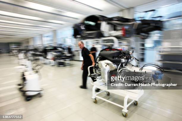 McLaren Automotive staff member moves a sports car engine and gearbox assembly on a wheeled trolley alongside cars under construction on the...