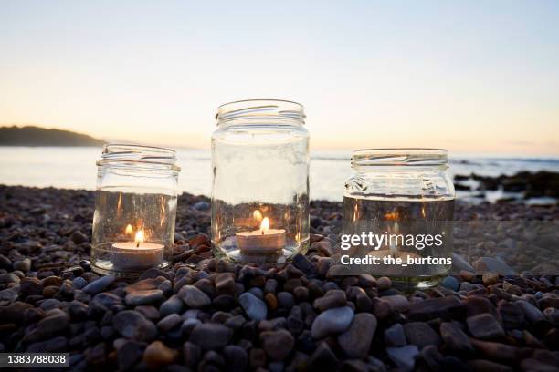 still life of tea lights in jars at beach at sunset - tealight stock pictures, royalty-free photos & images