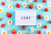 Summer month June text on light box and strawberry, chamomile flowers on blue background. Top view Flat lay. Creative concept Hello June. Top view, Flat lay, greeting card