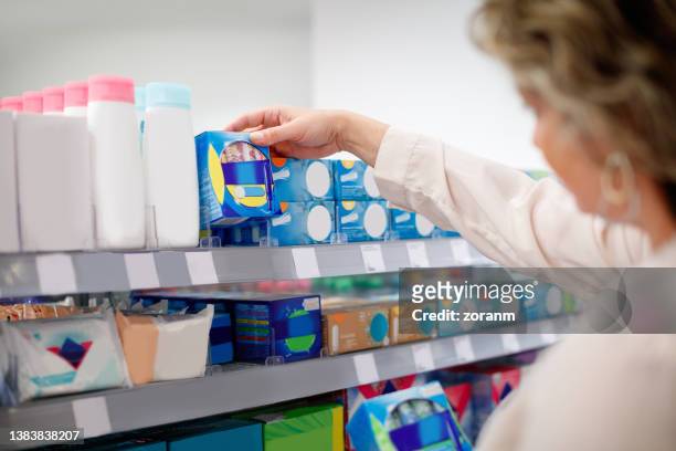 woman taking sanitary pads from shelf in the supermarket - tampon stock pictures, royalty-free photos & images