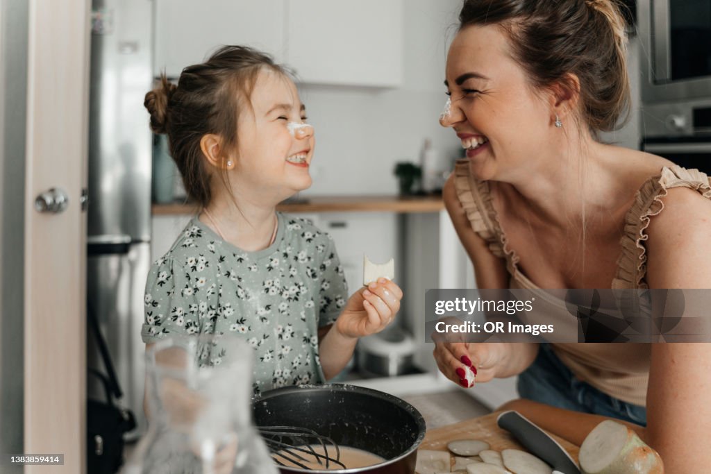 Playful mother and daughter preparing food together in kitchen