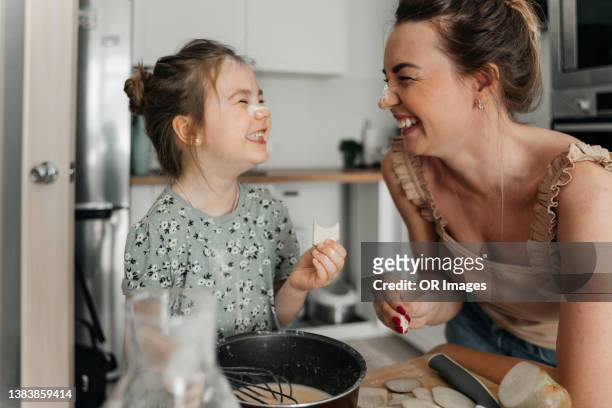playful mother and daughter preparing food together in kitchen - cocinar fotografías e imágenes de stock