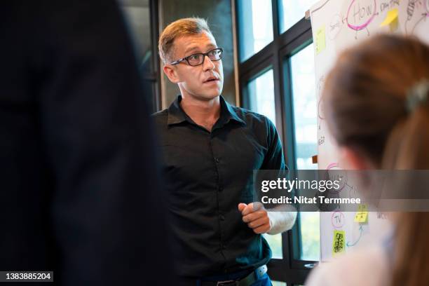 identify key features of a good presentation in business meeting. shot of male project leader during project meeting about project follow up with his team in the tech business office. - loyaliteit stockfoto's en -beelden