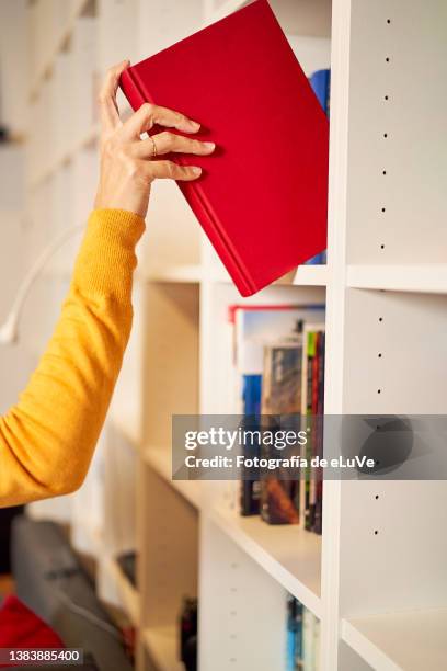 in the home an mixed race woman took a book off the shelf with her hand. - differential focus education reach stockfoto's en -beelden
