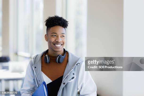 young man with headphones around neck smiles and looks away - headphone man on neck stockfoto's en -beelden