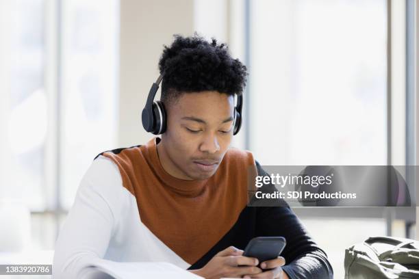 serious teen boy is distracted by phone - high school boys stock pictures, royalty-free photos & images