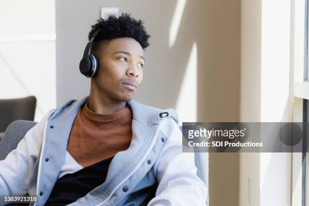 depressed teen boy listens to music on wireless headphones - african american teen stockfoto's en -beelden