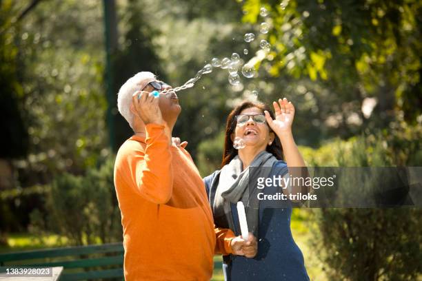 senior couple blowing bubbles at park - happy couple stock pictures, royalty-free photos & images