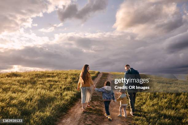 family walking on a rural dirt road at dusk - four people foto e immagini stock