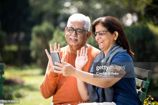 senior couple on video call at park - indian elderly couple stock pictures, royalty-free photos & images