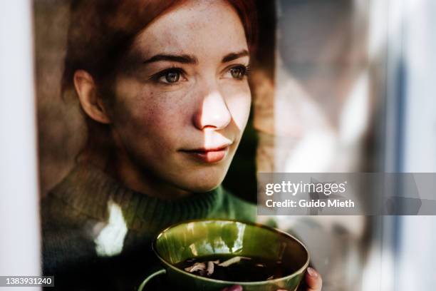 woman drinking tea while looking out of a window. - women tea stockfoto's en -beelden