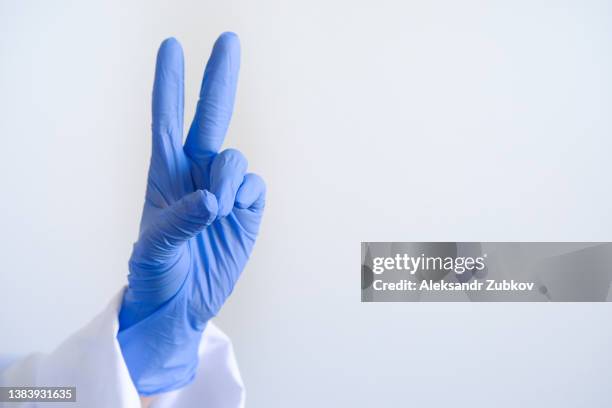 a human hand in blue surgical gloves, showing the victoria gesture. the doctor or medical professional shows a gesture, middle and index finger up. sign v. the concept of victory over the disease. healthcare and medicine. - latex 個照片及圖片檔
