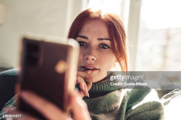 woman with red hair looking on screen of her mobile phone. - online messaging photos et images de collection