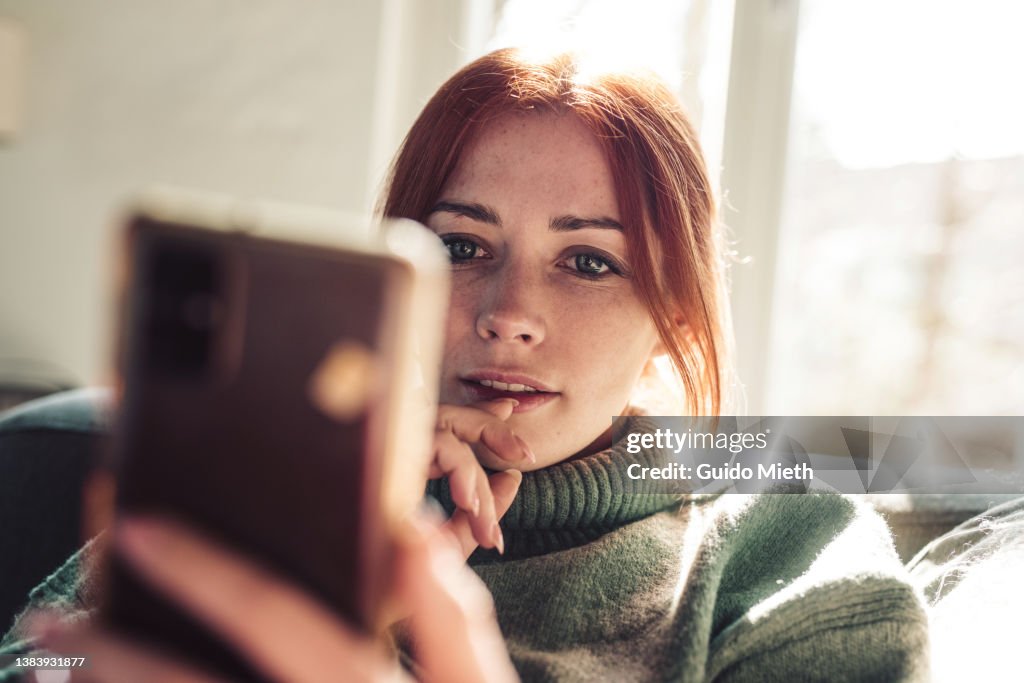 Woman with red hair looking on screen of her mobile phone.
