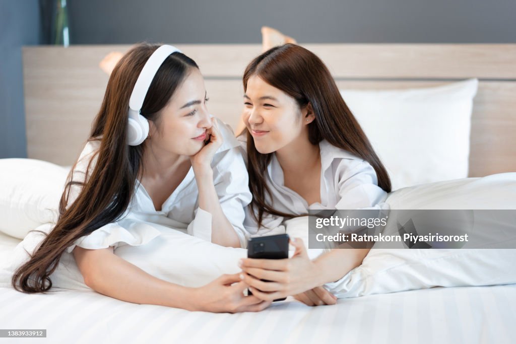 Asian Young Lesbian Couple Lover Dressing White Pajamas on Bed at home with Romantic Moment, LGBTQI Concept