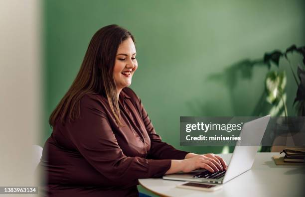 portrait of a happy plus size businesswoman using her laptop for work at home - plus size stock pictures, royalty-free photos & images