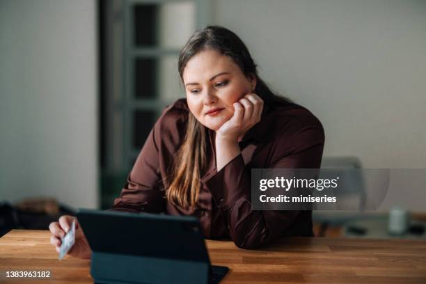 retrato de una hermosa mujer de talla grande usando su tarjeta para compras en línea - chubby credit fotografías e imágenes de stock