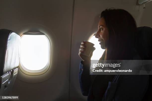 happiness latin business woman traveling by an airplane while drinking a cup of coffee during the fly. - passenger cabin stock pictures, royalty-free photos & images