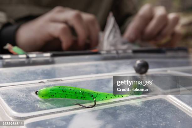 green fishing soft silicone bait for catching fish with a jig. artificial fishing tackle on a plastic box along with a sinker close-up - sinker stock pictures, royalty-free photos & images