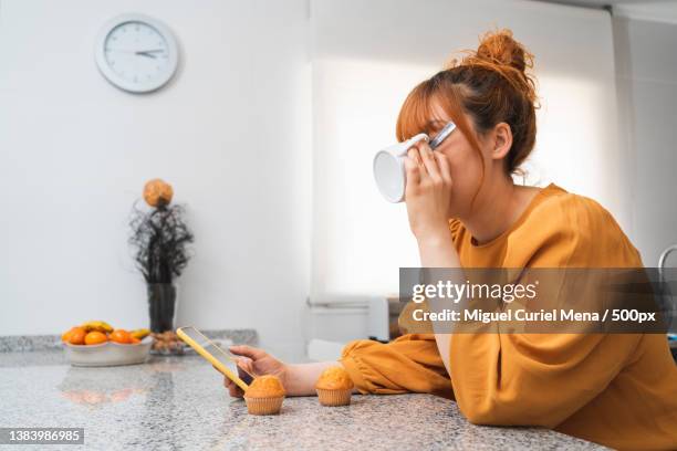 woman drinking tea in a kitchen while looking at her mobile phone,spain - yellow blouse stockfoto's en -beelden
