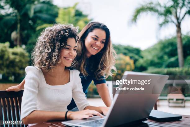 mother and daughter using laptop at swimming pool area - mother daughter hispanic stock pictures, royalty-free photos & images