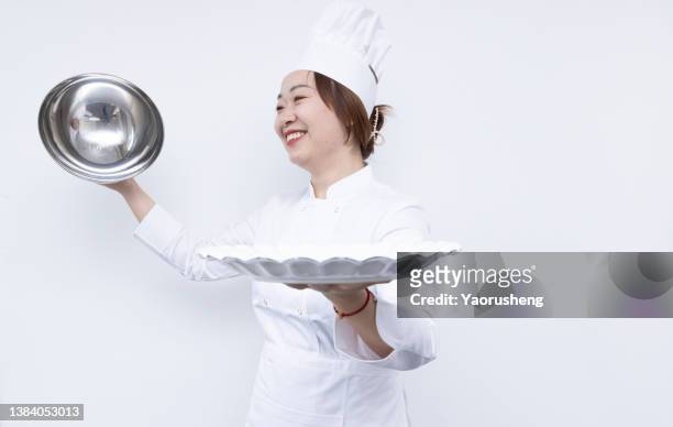 asian female chef wearing a chef's hat and carrying a domed tray and holding a empty plate. advertisement material - frau mit tablett stock-fotos und bilder