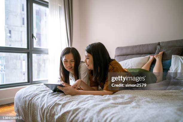 mãe e filha asiáticas deitadas na cama usando tablet digital em casa - chinese mothers day - fotografias e filmes do acervo