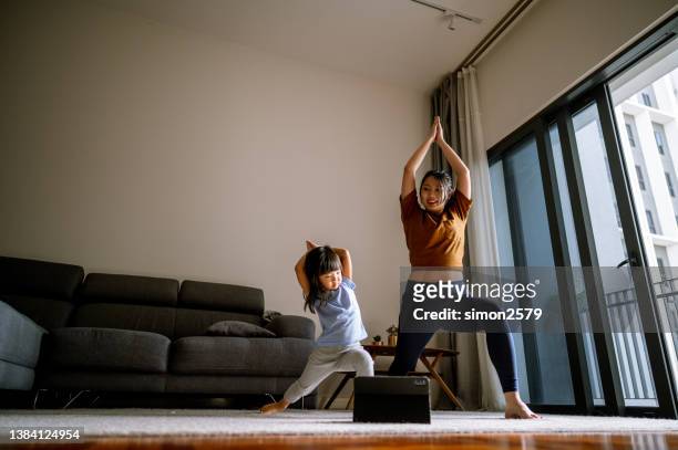asian mother and little girl are doing sport exercises with laptop at home - asian mum stockfoto's en -beelden