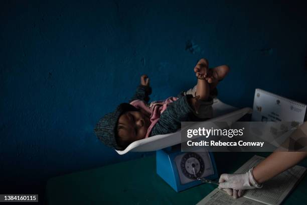 Nepali health care worker weighs an eight month-old baby suffering from malnutrition, and who has been prescribed fortified baby food to try to...