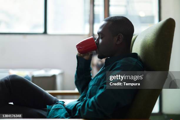 a young man is sitting at home drinking coffee. - black mug stock pictures, royalty-free photos & images