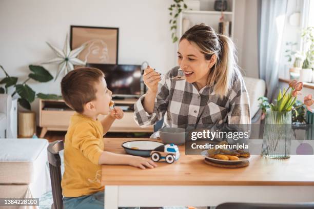 kleiner junge und mutter frühstücken - baby spielt mit essen stock-fotos und bilder