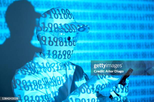 an unrecognisable person with a mask and binary code on his clothes is writing something in a mobile phone. robots programming. - security code stock pictures, royalty-free photos & images