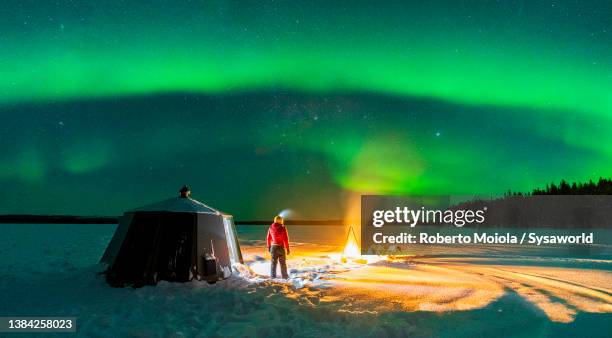 hiker watching northern lights out of glass igloo, lapland - iglu fotografías e imágenes de stock