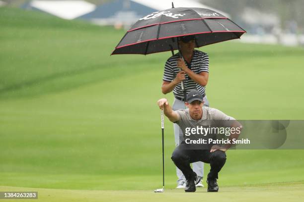 Justin Thomas of the United States holds an umbrella as Rory McIlroy of Northern Ireland lines up a putt on the ninth green during the continuation...