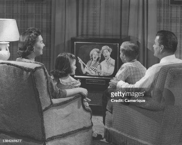 Mom, Dad, boy and girl well dressed siting in the living room watching a TV show.