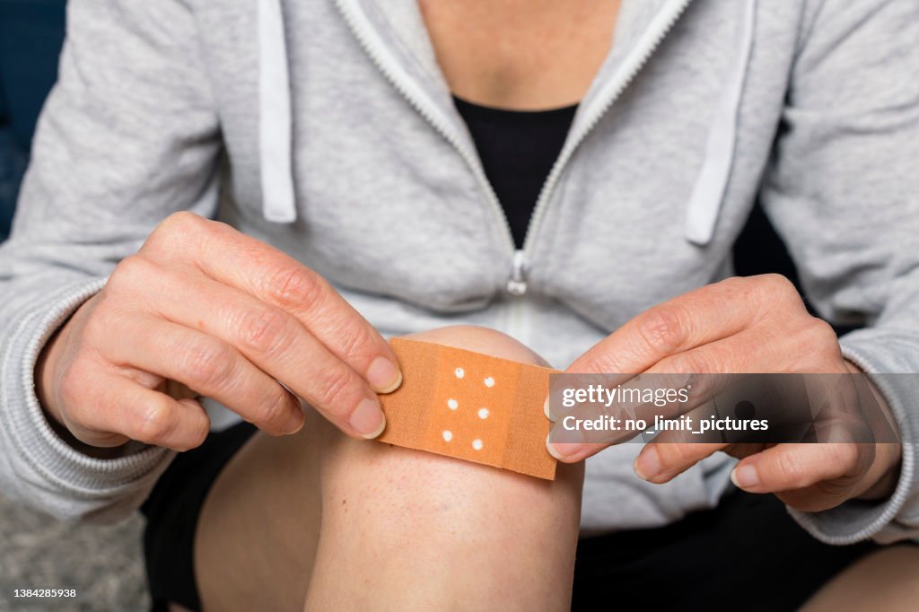 Frau klebt ein Pflaster auf ihr verletztes Knie
