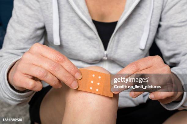 woman sticks a plaster on her injured knee - injured knee stock pictures, royalty-free photos & images