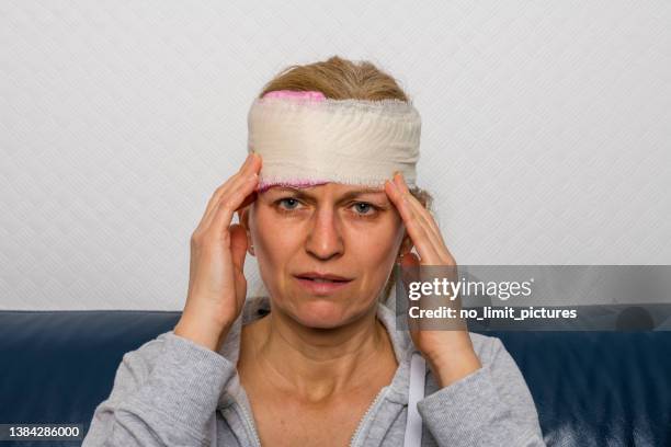 frau mit bandagen am verletzten kopf sitzt auf einer couch - head bandage stock-fotos und bilder